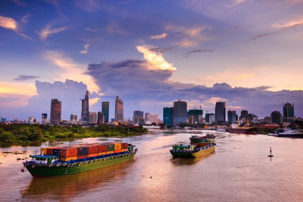 Container ships navigate the scenic Saigon River with Ho Chi Minh City skyline at dusk.