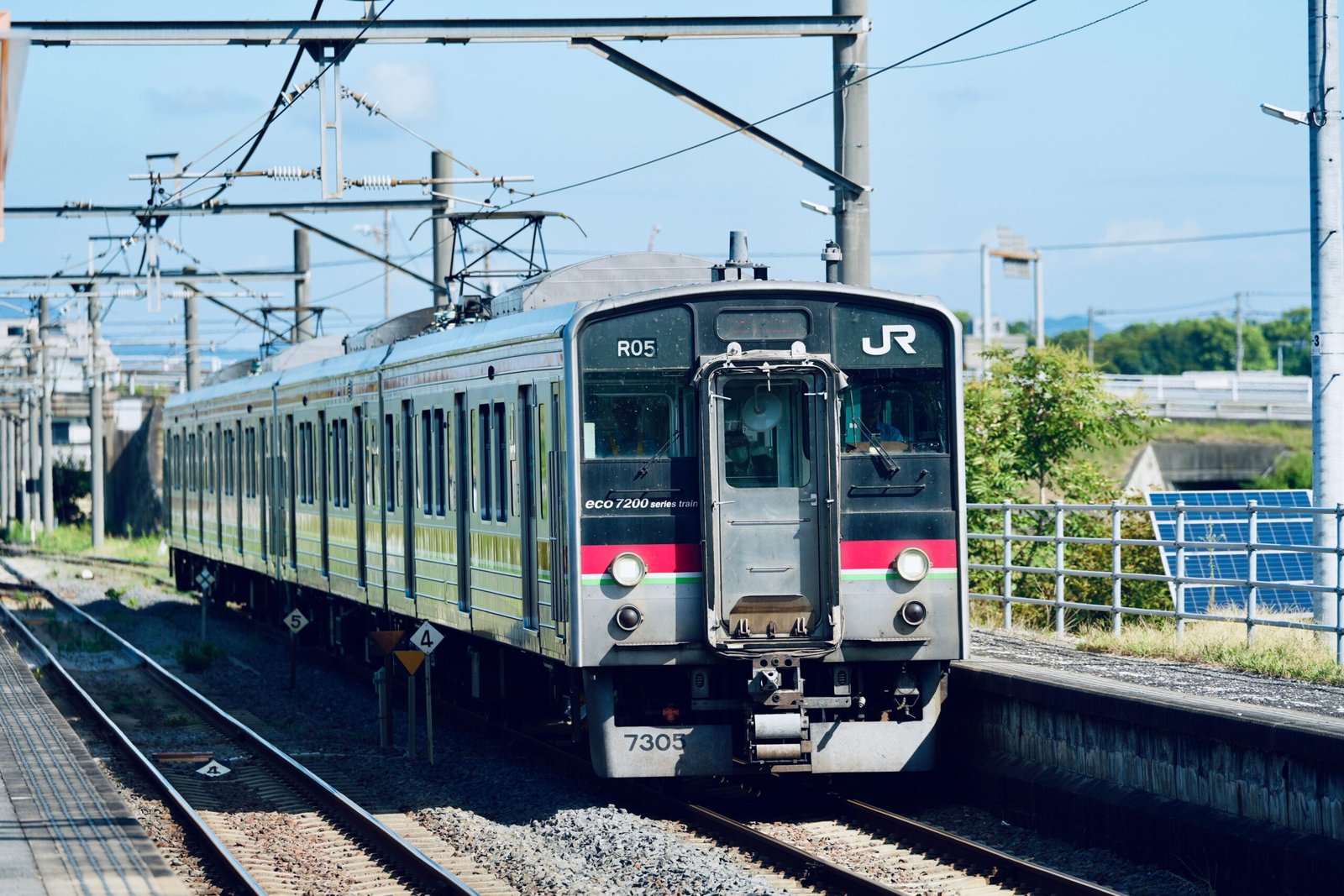 A JR commuter train travels on sunny tracks, showcasing modern transportation.