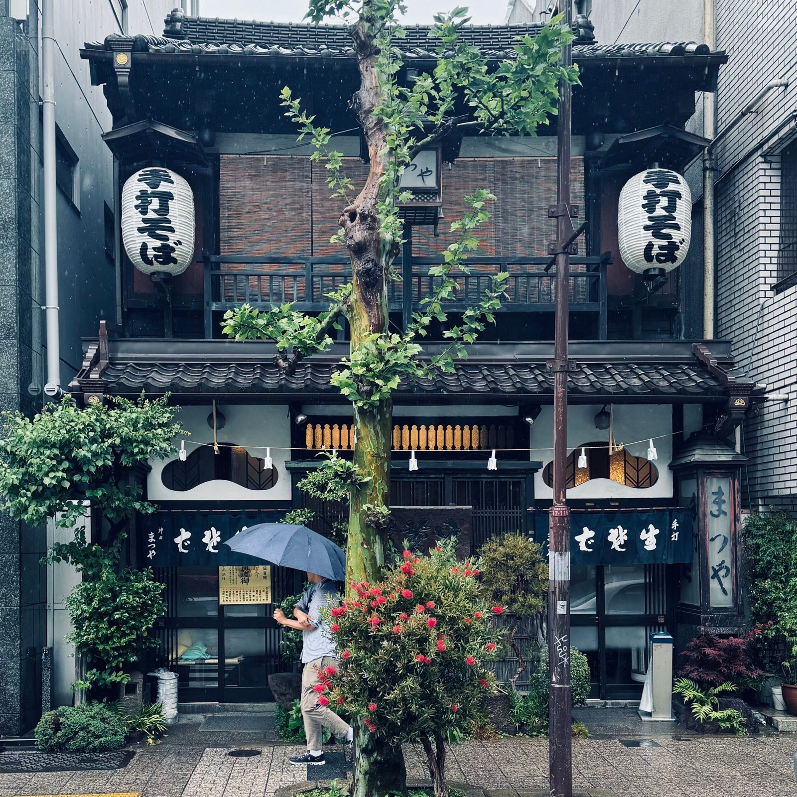 Rain-soaked day in front of a traditional Japanese restaurant with a passerby under an umbrella.