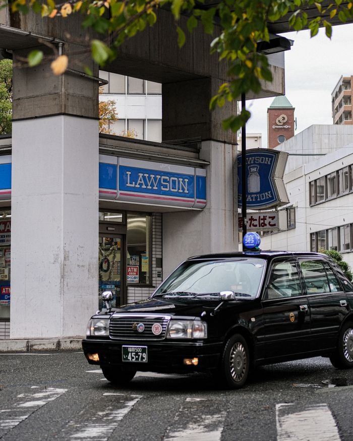 A black taxi is parked outside a Lawson convenience store on a city street in Japan.