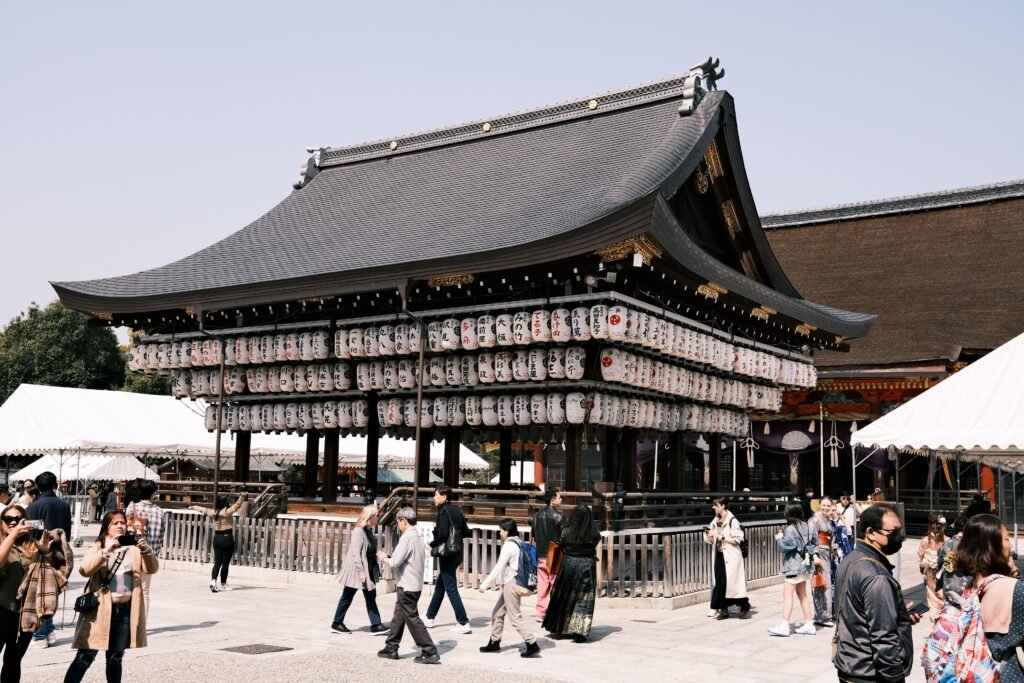 Visitors exploring Yasaka Shrine in Kyoto, decorated with traditional lanterns, under sunny skies.