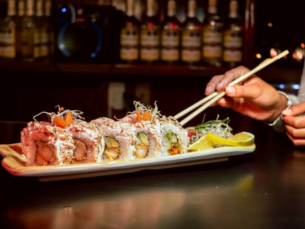 Close-up of gourmet sushi rolls with chopsticks in a cozy bar setting, highlighting fresh ingredients.