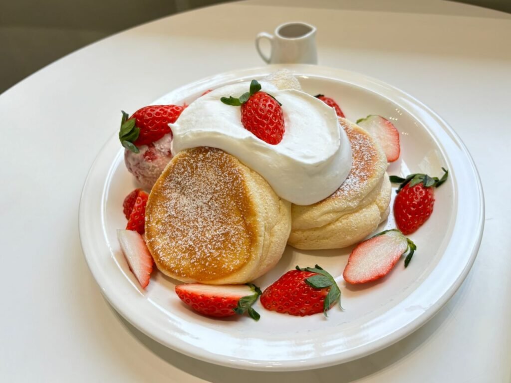 Delicious plate of fluffy Japanese souffle pancakes topped with fresh strawberries and cream.