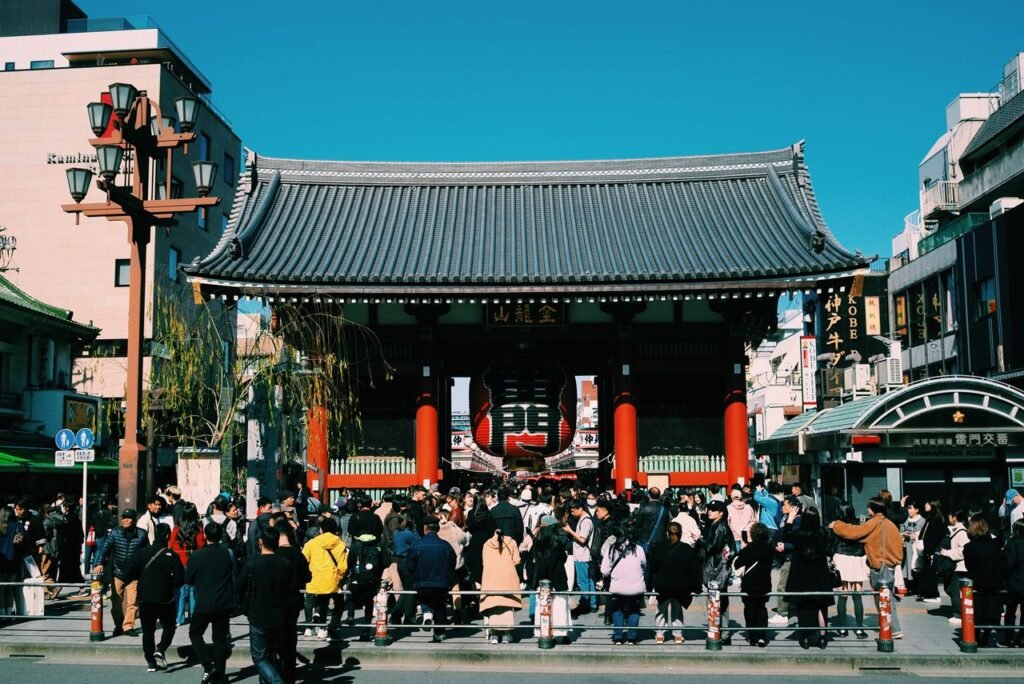 Large crowd gathers at the iconic Senso-ji Temple gate in Tokyo, Japan, under a clear blue sky.