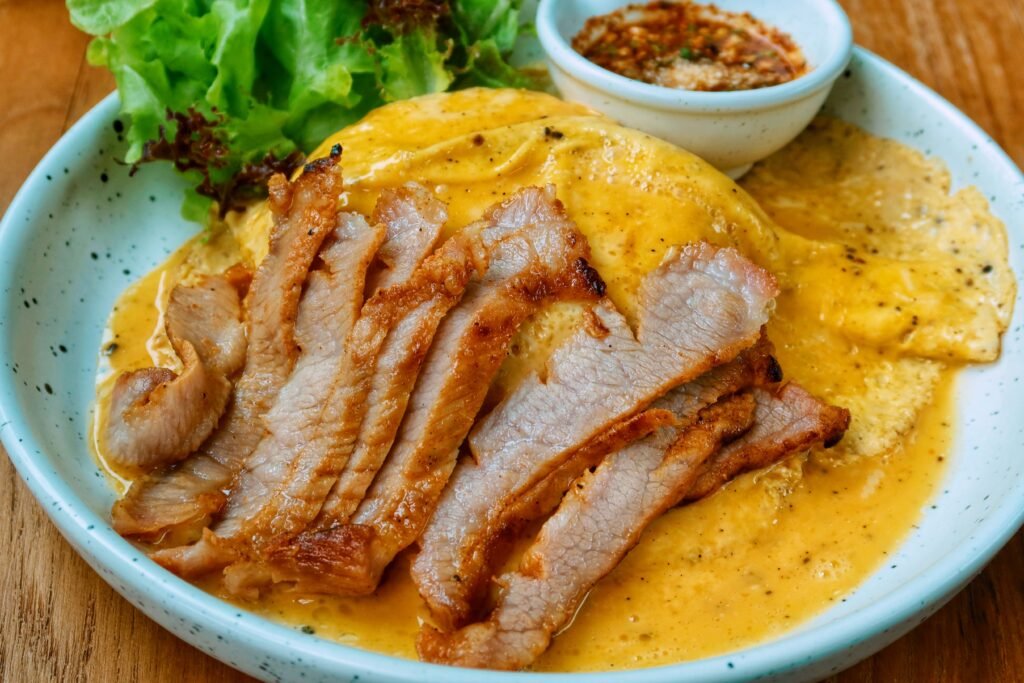 Close-up of pork slices on an omelette with spicy dipping sauce and greens.