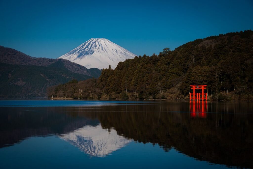 Stunning view of Mount Fuji and a red torii gate reflecting in Lake Ashi, Hakone, Japan.